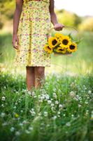 Woman wearing a yellow flowery dress holding a trug of Sunflowers in a meadow