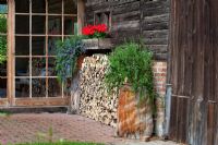 House entrance with glass door, wood pile, a window box with Zonale Pelargonium and Rosmarinus officinalis