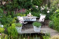 Decked patio next to pond. Lychnis coronaria, Achemilla mollis and Rosa 'Astrid Lindgren' - Scheper Town Garden 