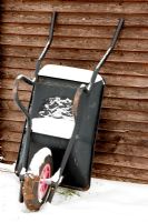 Wheelbarrow leant against shed covered in snow