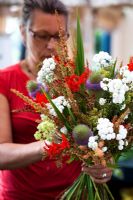 Woman arranging bunch of Crocosmia 'Lucifer', Wild Teasel, Rumex - Dock Flowers, Achillea ptarmica 'The Pearl' - Growing Together Nursery 
 