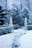 Formal town garden with wooden obelisks covered in snow, Oxford, UK. 
