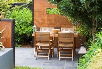Small town garden with wooden table and chairs, lantern, screens made of mild steel, decking and raised bed, London
