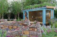 Modern summerhouse in garden with dry stone walls and insect habitats 