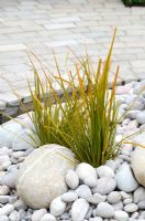 Ornamental grass growing in pebbles, next to a water rill - LOROS Hospice Garden of Light and Reflection, Silver Medal Winner, RHS Hampton Court Flower Show 2011
