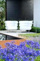 White chairs on a black and white pavilion next to a Cor-Ten steel water trough surrounded by Agapanthus and Stipa tenuissima and Box hedging . 'Vestra Wealth's Gray's Garden', Gold Medal Winner, RHS Hampton Court Flower Show 2011 