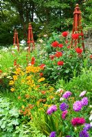 Decorative border punctuated by red wooden obelisks featuring brightly coloured dahlias, Rudbeckia 'Marmalade', Aster 'Ostrich Plume Mixed', Cosmos 'Purity', crocosmias and an edging of Alchemilla mollis