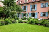 An ancient stable has been transformed into a modern family house in traditional style with blue window shutters and a formal garden, with old Apple tree and Rosa 'Pierre de Ronsard' - Freising, Germany