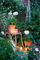 Glass jar tealights lighting up Geraniums in containers in white garden