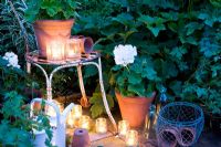 Glass jar tealights lighting white geraniums in containers in white garden