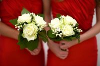 bridesmaids in red dresses holding bouquets of white roses