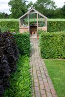 Brick pathway leading to greenhouse, through Fagus Beech hedges 