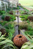 Rill garden behind farmhouse with terracotta spheres and plants including Phormium tenax, Potentilla fruticosa 'Primrose Beauty', Erica carnea 'Springwood White', Dorset
