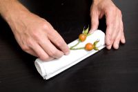 Man rolling napkin with decorative seed heads 