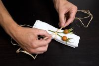 Man tying decorative seed heads to napkin 