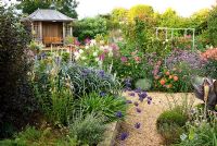 Central pond and summerhouse feature in the sunken garden, constructed in 2005, surrounded by a colourful mass of perennials and annuals including Eucomis, Verbena bonariensis, Dahlias, Agapanthus, Cleomes and dark leaved Cannas with gravel paths giving access - Isle of Wight, UK