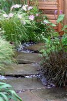 Stone pathway through mixed border with ornamental grasses 
