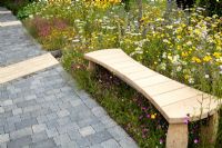 Timber bench surrounded by Anthemis, Achillea and Ox-eye daisies. Path of stone setts - 'Stitch in Time Saves Nine' garden - RHS Tatton Park Flower Show 2011 
