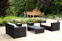 Suburban family garden in early autumn with contemporary furniture on sandstone patio. Childrens play area next to lawn. Fagus - Beech hedge and mixed borders of Cosmos, Stipa tenuissima
