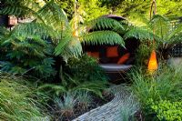 Contemporary light and covered seat surrounded by Dicksonia antarctica and Polystichum setiferum ferns 