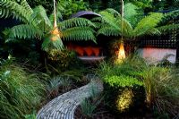 Contemporary lighting and covered seating area surrounded by Dicksonia antarctica and Polystichum setiferum ferns in suburban garden 