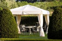 A canvas gazebo with metal table and chairs in formal country garden 