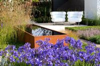Long metal water trough, with agapanthus, grasses, clipped box lawn, pavilion floor of cream limestone