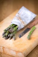 Asparagus spears wrapped in newspaper with knife on chopping board  