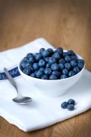 Blueberries in a white bowl on a tea towel with spoon