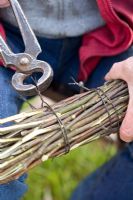 Making a Birch broom  - man tying up birch branches with steel wire using pliers.