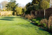 Herbaceous borders feature standard Quercus ilex - Holm Oaks underplanted with Crambe cordifolia, white Daisies, Nepeta 'Six Hills Giant', Stemmacantha centaureoides and Lychnis chalcedonica that emerge through woven hazel supports - Melplash Court, Bridport, Dorset, UK