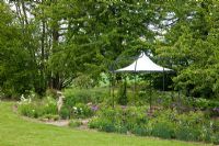 A pavilion and a female statue are features in a mixed border backed by trees - Prunus avium and Tulipa 'Queen of Night' - Jens Tippel