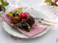 Table decoration of Ilex - Holly berries, Pinus - Pine cones and red baubles on pink napkin
