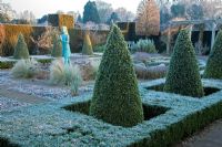 The formal knot garden with clipped box hedging and cone shaped pyramids. Statue of a girl holding the lamp of wisdom by Nathan David - Waterperry Gardens, Oxfordshire 