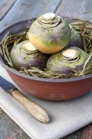 Brassica napus - Swedes in a ceramic bowl protected with raffia, on linen cloth with knife