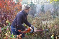 Woman cutting back herbaceous border with hedge cutter
