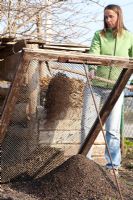 Woman sieving compost with shovel through the iron mesh to remove large lumps
