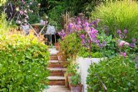 View up steps in terraced garden to patio with table and chairs