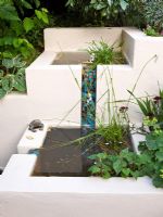 Water feature with rendered block walls of warm ivory - water trickles down a mosaic chute into basin below
