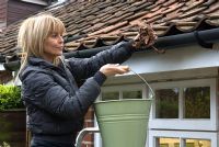 Woman on step-ladder removing dead leaves from cottage guttering