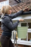 Woman on step-ladder removing dead leaves from cottage guttering