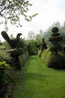 Yew Topiary birds, wedding-cake tiers and crowns, and wavy Buxus hedges frame enclosed grass pathway
