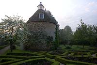 Pigeon House garden with pigeon house, 1685, and box parterre with Cornus nuttallii and new red leaves of hybrid tea roses. Rousham House