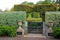 Gate into the Flower Garden is framed with a pair of urns, with clipped Euonymus trained against the wall, and fern Dryopteris affinis 'Cristata' planted at the base - Herterton House, Hartington, Northumberland, UK