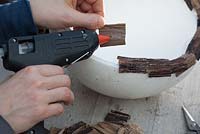 Person gluing pieces of bark around edge of bowl 
