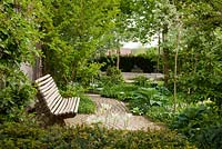 Wooden bench surrounded by Hosta, Prunus kurilensis 'Brilliant', Pyrus salicifolia, Taxus, Tulipa viridiflora 'Spring Green' and Vinca minor 'Alba' - Hollberg Gardens 