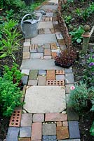 Cottage garden style path made with salvaged materials including slabs, bricks, concrete block pavers and pebbles 