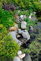 Planted flint water feature beside garden pond, Norfolk, UK, June