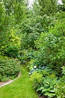 Bistro garden furniture next to borders with shrubs and perennials, Alchemilla mollis, Hosta and Paeonia