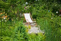 Deck chair on wooden deck in the margin zone of a garden pond with lush vegetation